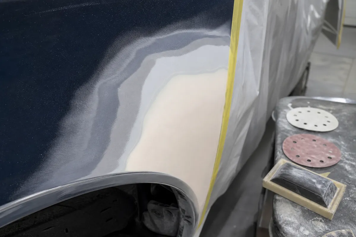 Close-up of a feathered automotive paint repair edge with old paint, primer, and filler smoothly blended