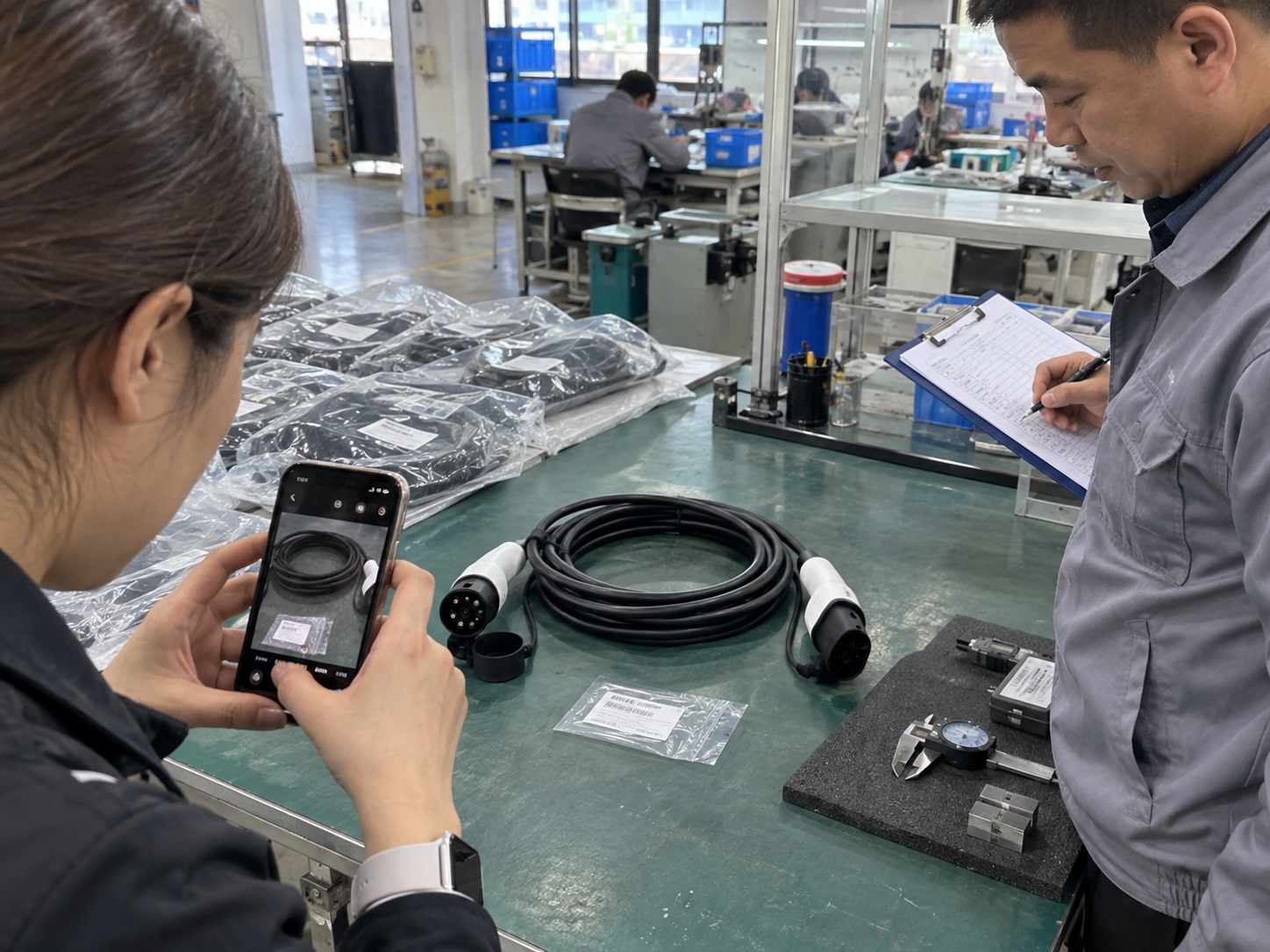 Buyer photographing batch labels and an EV charging cable while a QC manager checks a scorecard and retained samples