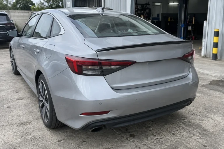 Silver sedan with a low trunk lip spoiler outside a workshop