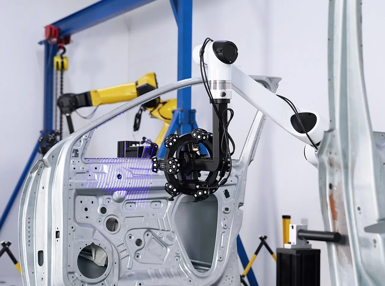 Robot-mounted optical 3D scanner measuring a car door panel (illustrative photo; Kelly No.715, CC BY-SA 4.0, Wikimedia Commons)