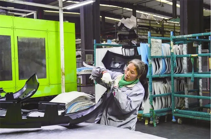 Operator handling a black injection-molded bumper part beside a molding machine in the Wuxi factory