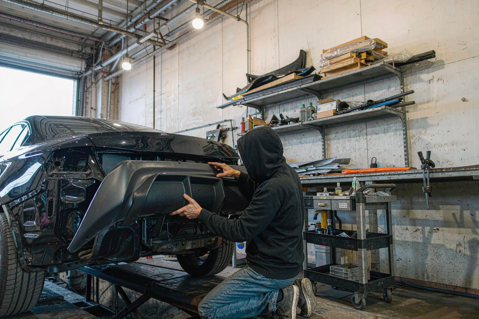 Solutions 2 Technician fitting a black rear diffuser to a car in a body shop