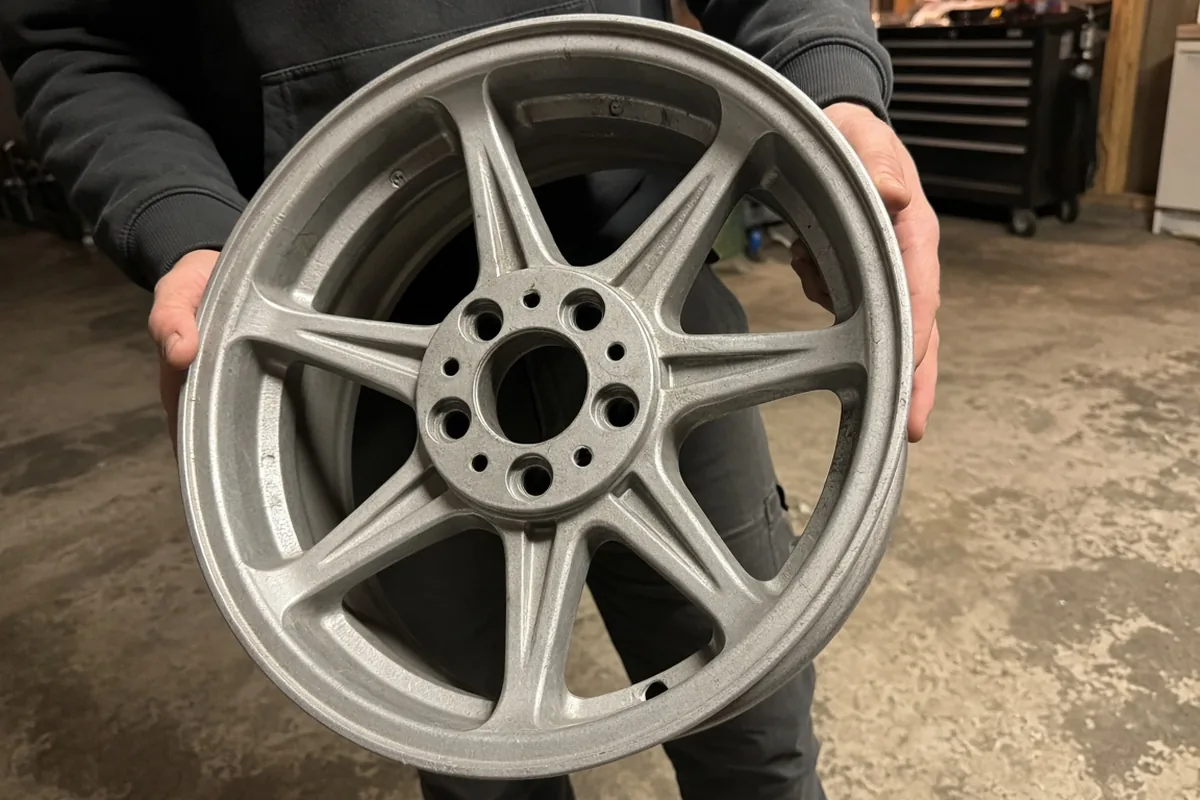 How to Measure Bolt Pattern and Center Bore Before Ordering Wheels 1 Person in a garage holding a bare silver multi-spoke alloy wheel upright, showing the front face, center bore and lug holes
