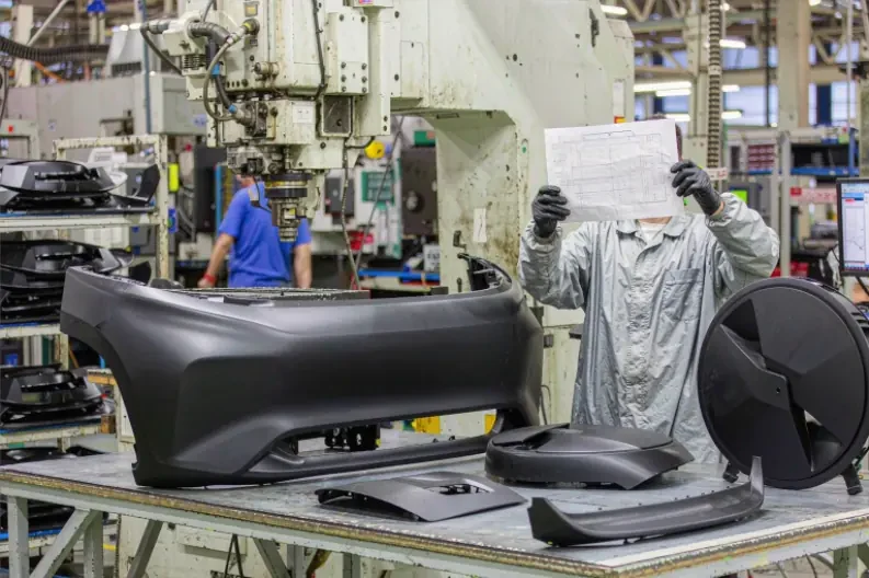 Engineer checking a drawing beside molded bumper and trim parts on the production line